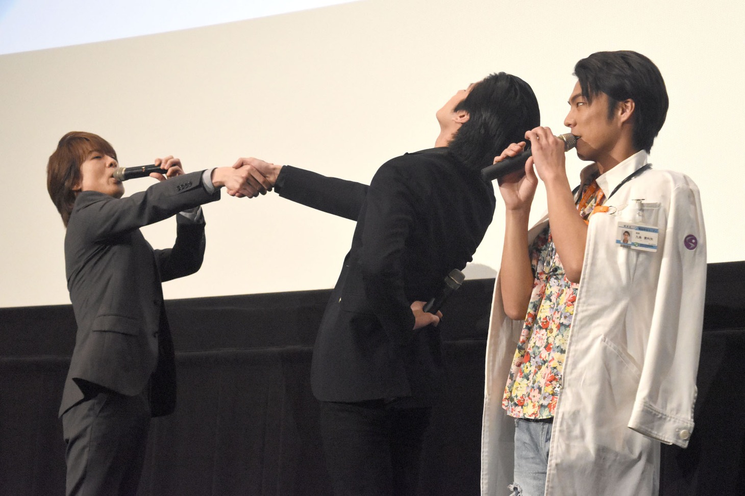 大げさに握手する貴水博之（左）と岩永徹也（中央）。