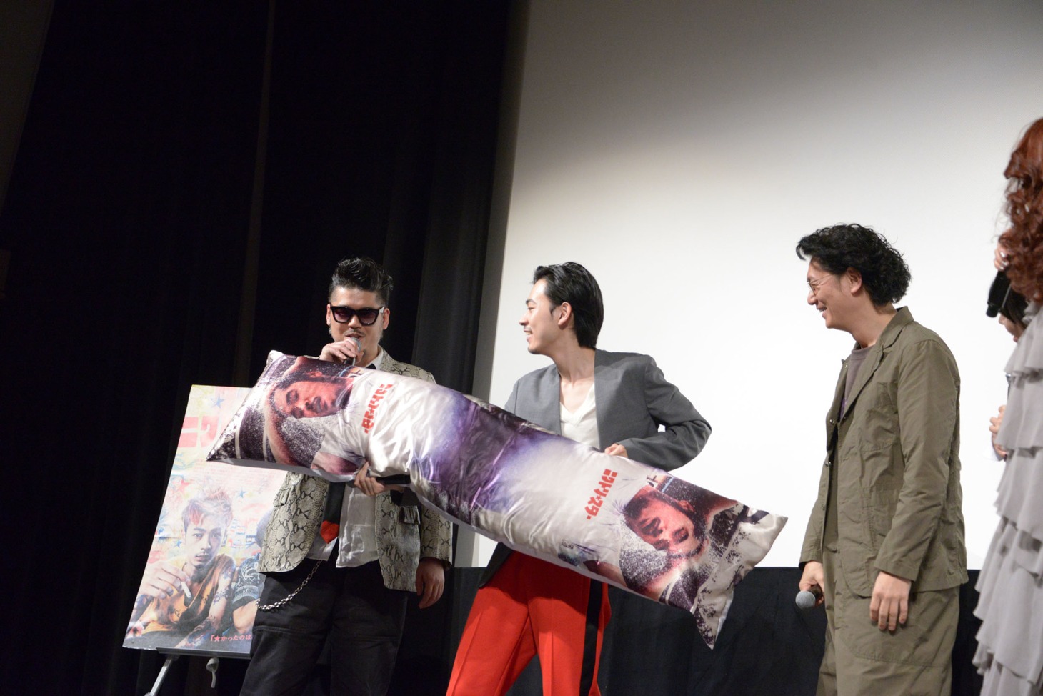 かなた狼（左）の監督デビュー作完成を祝し、成田凌（中央）と井浦新（右）から、かなたのブロマイドを使用した抱き枕が贈られる様子。