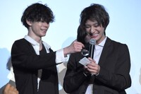 抽選会にて当選番号を読み上げる高崎翔太（右）と、ルーペを使って高崎の手助けをする玉城裕規（左）。