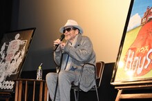 「花筐／HANAGATAMI」「HOUSE ハウス」のポスターに挟まれて座る大林宣彦。