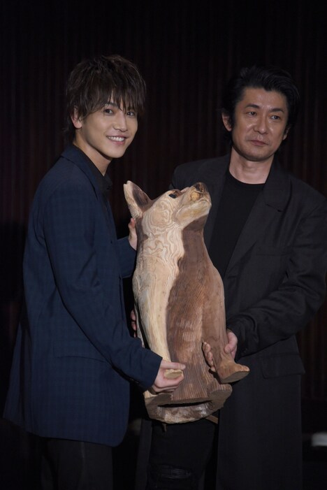 智の愛犬・コウの木彫りを抱く岩田剛典（左）と永瀬正敏（右）。