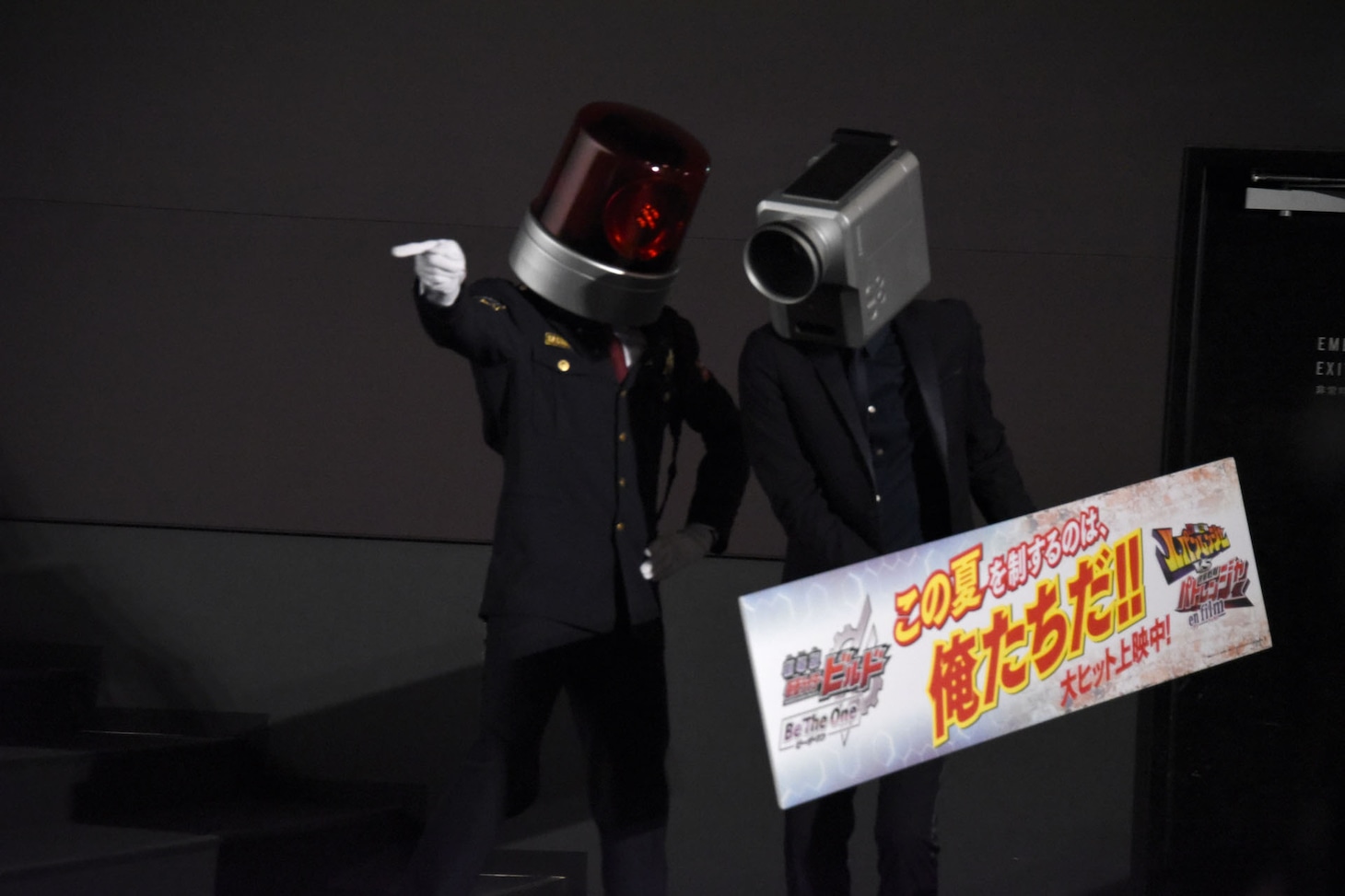 パネル運びを命じられるカメラ男（右）。