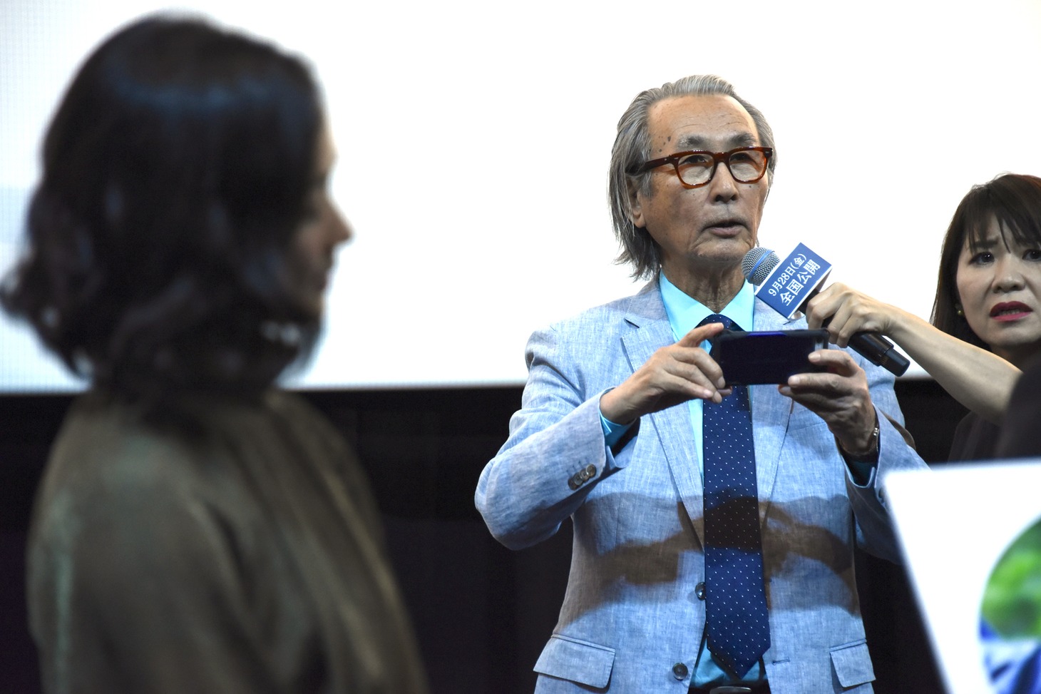 スマートフォンでキャストを撮影しようとする木村大作（中央右）。