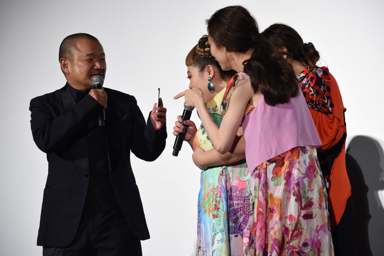 携帯電話でネットニュースを見る大根仁（左）のもとに、ぞろぞろと集まる“大人SUNNY”を演じたキャストたち。