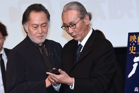 木村大作（右）のスマートフォンをのぞき込む北大路欣也（左）。