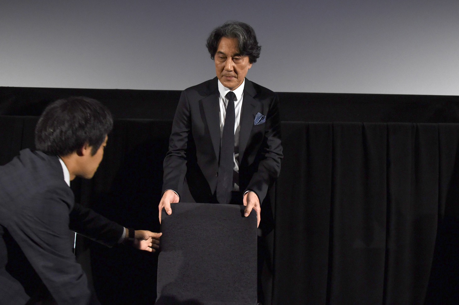 フォトセッション前に椅子の片付けを手伝う役所広司。