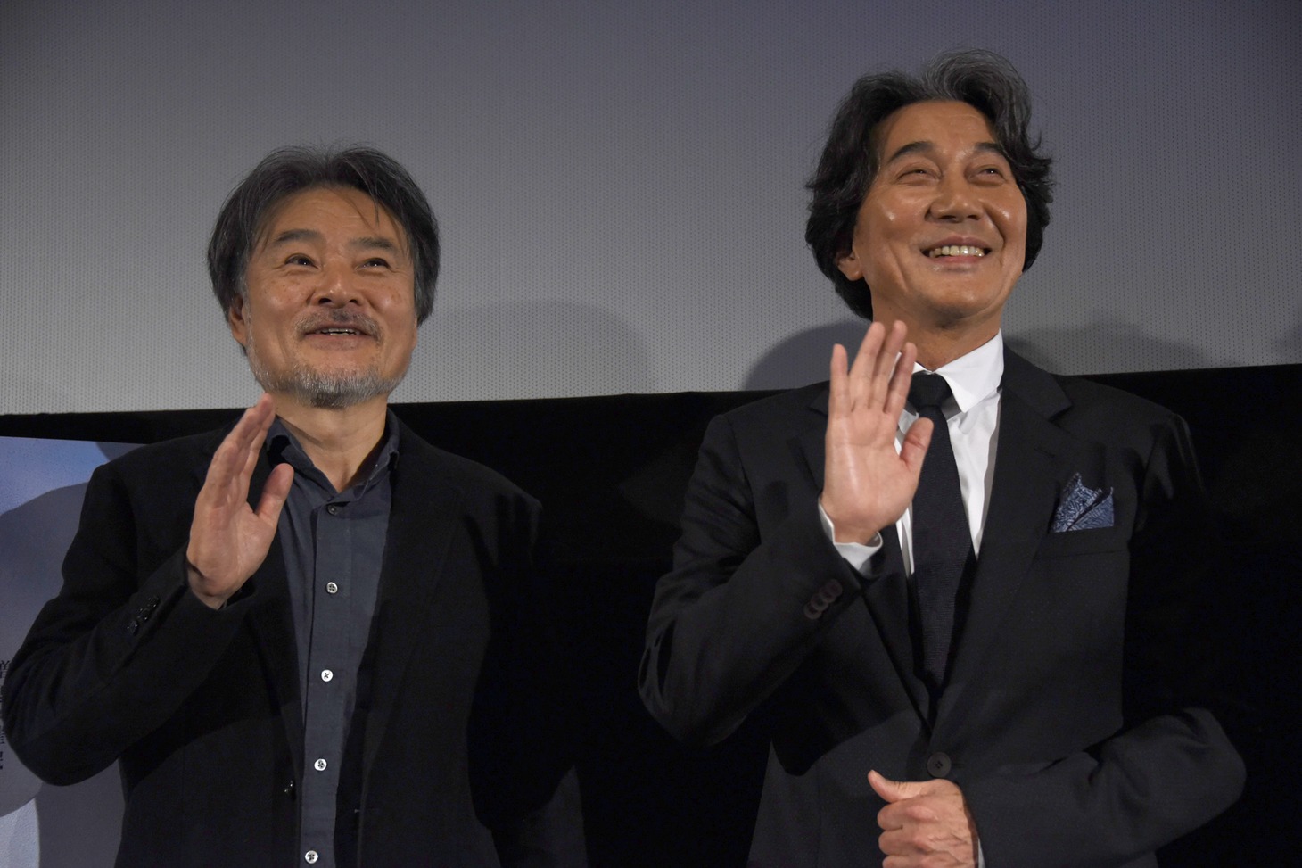 ムービーカメラに手を振る黒沢清（左）と役所広司（右）。