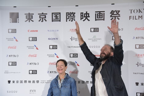 ムービーカメラへ大げさに手を振るレイフ・ファインズ（右）。