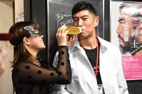 M女のウラン（左）から哺乳瓶でお茶を飲ませてもらう高嶋政宏（右）。