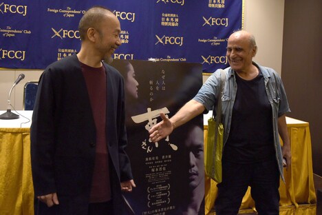 写真撮影に応じている塚本晋也(左)のもとへ近寄り、握手を求めるアミール・ナデリ(右)。