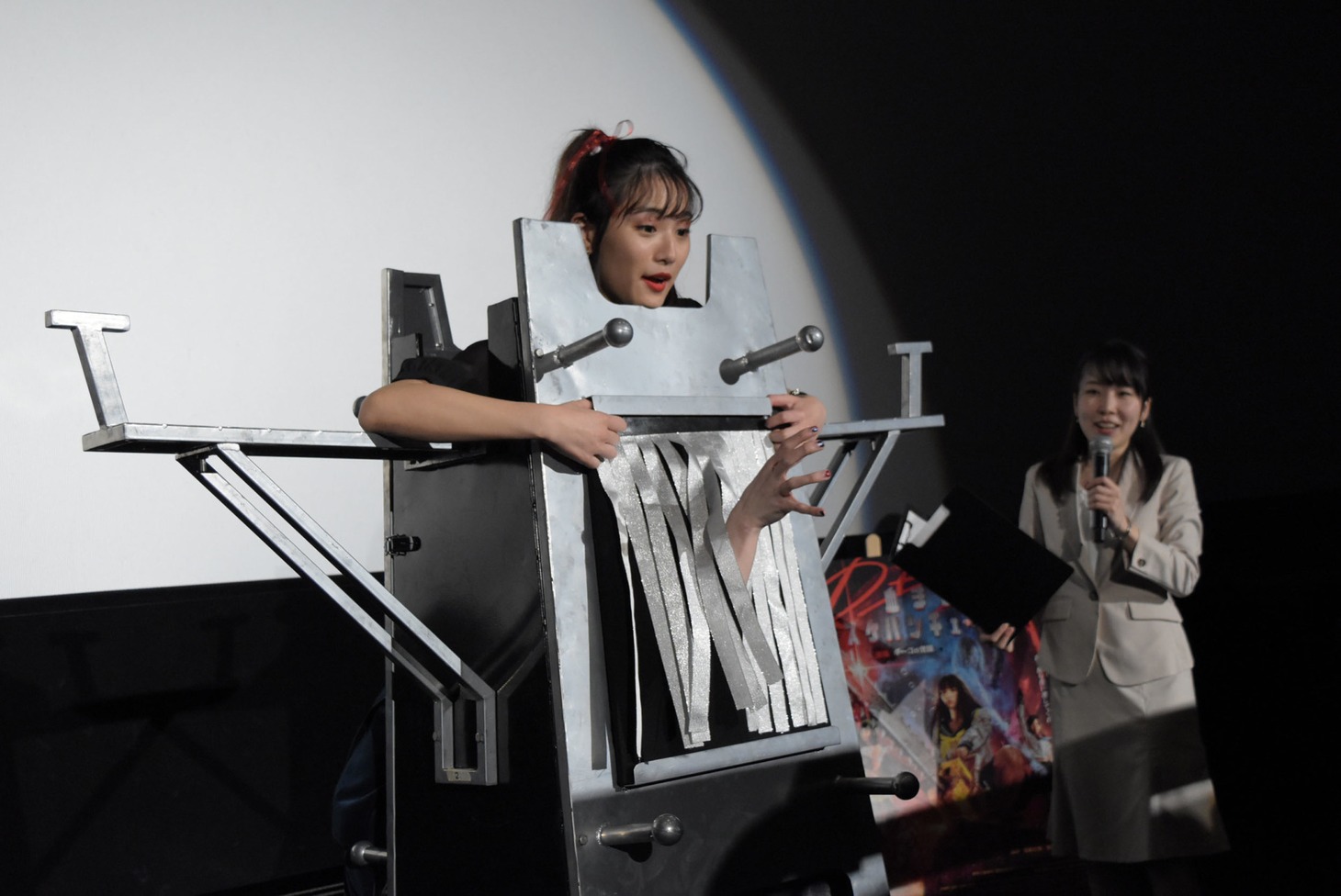 装置の背後から浅川梨奈の体を貫き、あのの手が現れた様子。