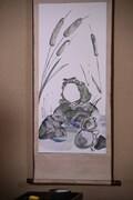 掛け軸の中のカエルの姿をしたガマノ師匠。
