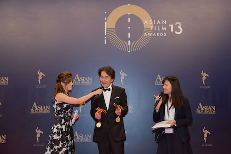 司会者に今後の抱負を聞かれ、トロフィーで筋トレを始める役所広司（中央）。