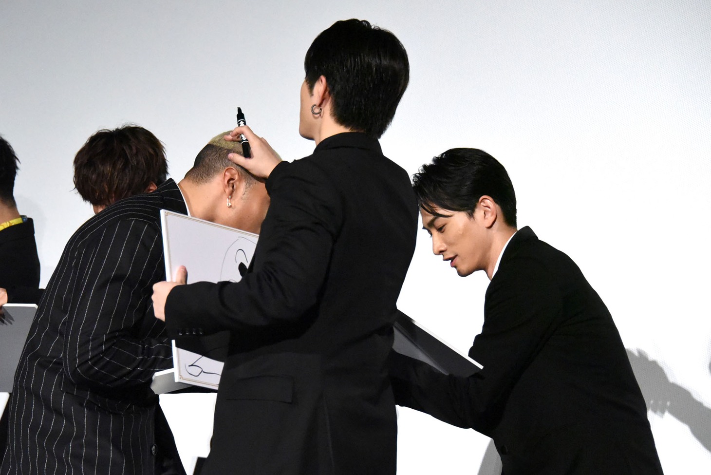 関口メンディー（左）の頭皮を見ながら、白石聖の似顔絵を描く佐野玲於（手前）。