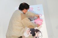 ポスターパネルに公開日の書かれたシールを貼る片渕須直監督。