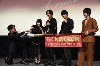 重さ30kgの矛を使用したフォトセッションの様子。矛から手を放しファイティングポーズを取る橋本環奈（中央左）と山崎賢人（中央）にツッコむ吉村崇（左）。