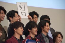 カメラマンの指示に従い、「刮目」と書いたスケッチブックの位置を微調整する南圭介。