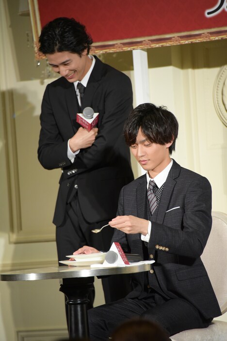 罰ゲームとしてスープを飲む際の正しいマナーを実演してみせる永瀬廉(手前)とそれを笑って見守る清原翔(奥)。