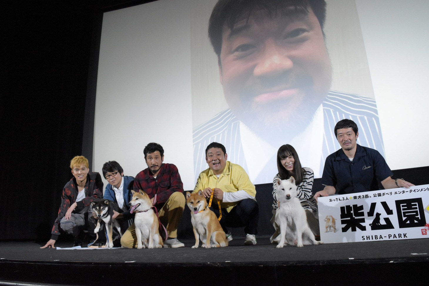 「柴公園」初日舞台挨拶にて、左から水野勝、大西信満、渋川清彦、ドロンズ石本、桜井ユキ、綾部真弥。背景は佐藤二朗のVTR映像。