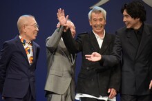 かたくなに手を振ろうとしない橋爪功（中央左）の手を取って振らせる田中民（中央右）。