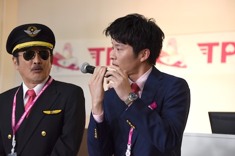 機内アナウンス用マイクの持ち方を再現する田中圭（右）。