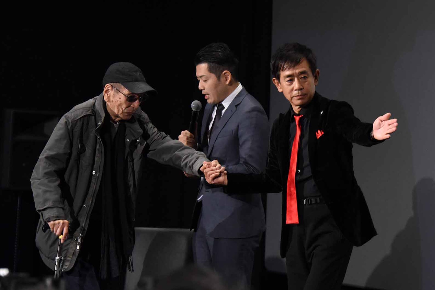 小林清志（左）の手を引いて登壇する栗田貫一（右）。