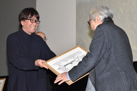 高橋陽一（左）がコラボイラストを山田洋次（右）に渡す様子。