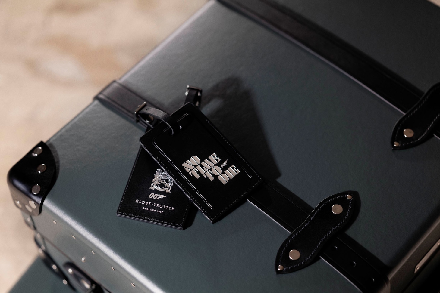 “No Time To Die”コレクションのグローブ・トロッターとネームタグ。Photographed by Greg Williams at The Rosewood Hotel