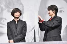 ムービーカメラに気付かない川上洋平（左）へ、パネル越しに合図を送る綾野剛（右）。