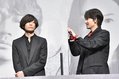 ムービーカメラに気付かない川上洋平（左）へ、パネル越しに合図を送る綾野剛（右）。