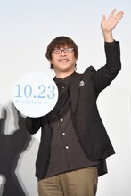 手持ちパネルと左手を振る三木孝浩。