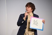 「越」と書かれたフリップを持つ三木孝浩。