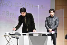 筆を執る岩田剛典（左）とそれを見守る新田真剣佑（右）。