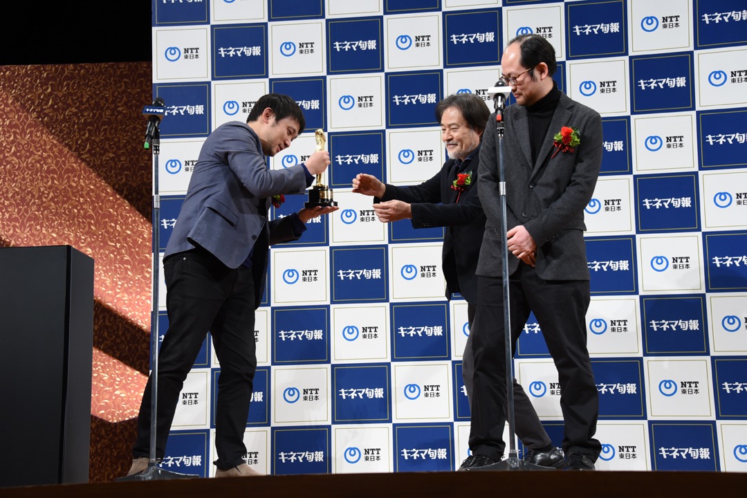 自分の挨拶が終わり、黒沢清（中央）にトロフィーを渡す濱口竜介（左）。