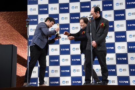 自分の挨拶が終わり、黒沢清（中央）にトロフィーを渡す濱口竜介（左）。