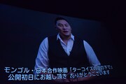 スクリーンに映し出されるアムラ・バルジンヤムのメッセージ映像。