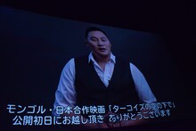 スクリーンに映し出されるアムラ・バルジンヤムのメッセージ映像。