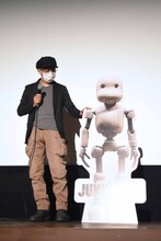 パートンのパネルに手を置く堀貴秀。劇中でパートンの身長は140cmと想定されており、パネルはその高さとなっている。