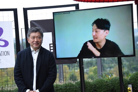 是枝裕和（左）に、画面越しに手を振るチャン・チェン（右）。