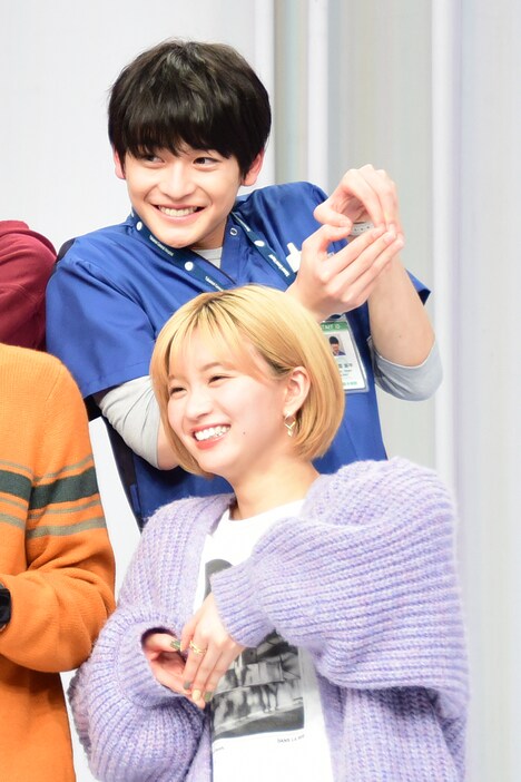 手でハートマークを作る岡崎紗絵（手前）、高橋文哉（奥）。