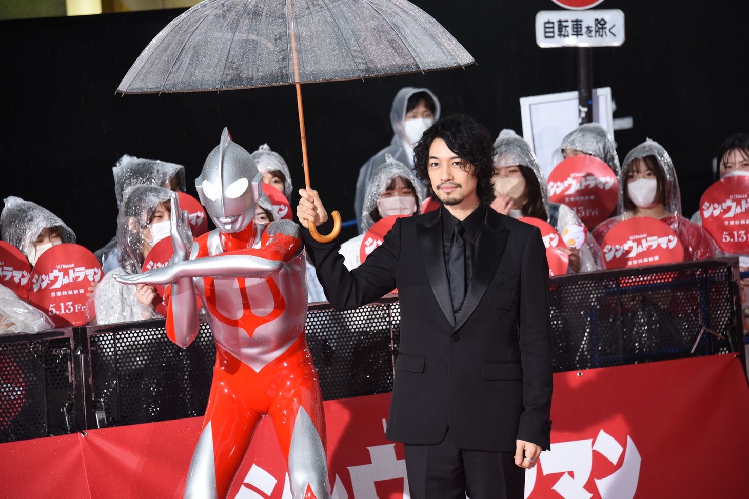 ウルトラマン（左）が濡れないよう傘に入れる斎藤工（右）。