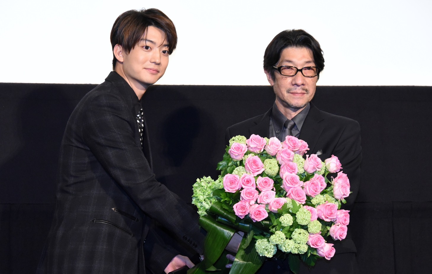 伊藤健太郎（左）から花束を受け取る阪本順治（右）。