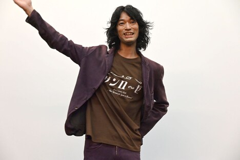 主題歌「サンローゼ」のロゴが入ったTシャツをアピールする、こだまたいち。