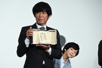 第76回カンヌ国際映画祭で受賞した脚本賞のトロフィーを手にする坂元裕二（前）とのぞき込む柊木陽太（後ろ）。