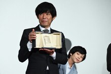 第76回カンヌ国際映画祭で受賞した脚本賞のトロフィーを手にする坂元裕二（前）とのぞき込む柊木陽太（後ろ）。