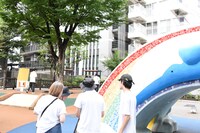 話し合いが続く赤チームを遠くから撮影する真利子哲也（中央）。