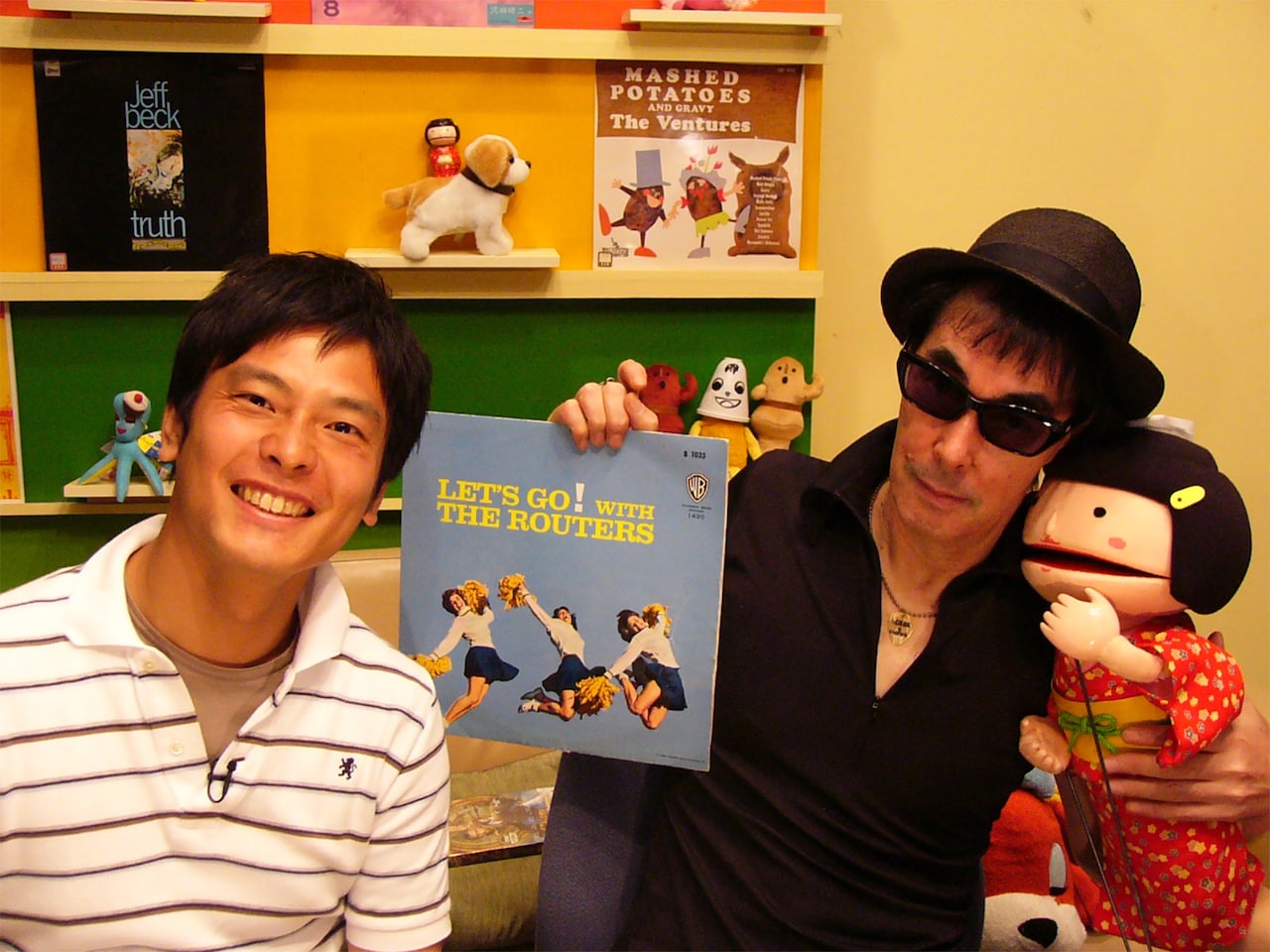 「チャートバスターズR！」ゲスト出演時の様子。左から田畑竜介、鮎川誠、こけてぃっしゅ隊員。鮎川が手にするレコードはザ・ルーターズの「Let's Go! With the Routers」。