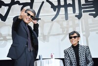 銃の構え方を披露する舘ひろし（左）と、その様子を見守る柴田恭兵（右）。