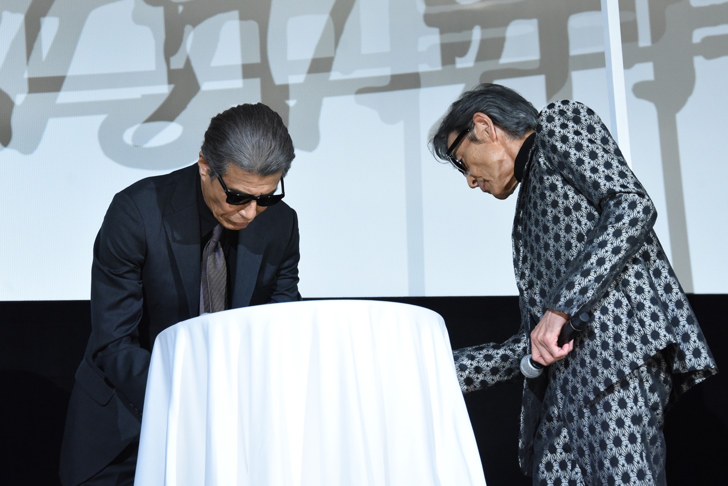 テーブルに隠された電話器を取り出す舘ひろし（左）と柴田恭兵（右）。