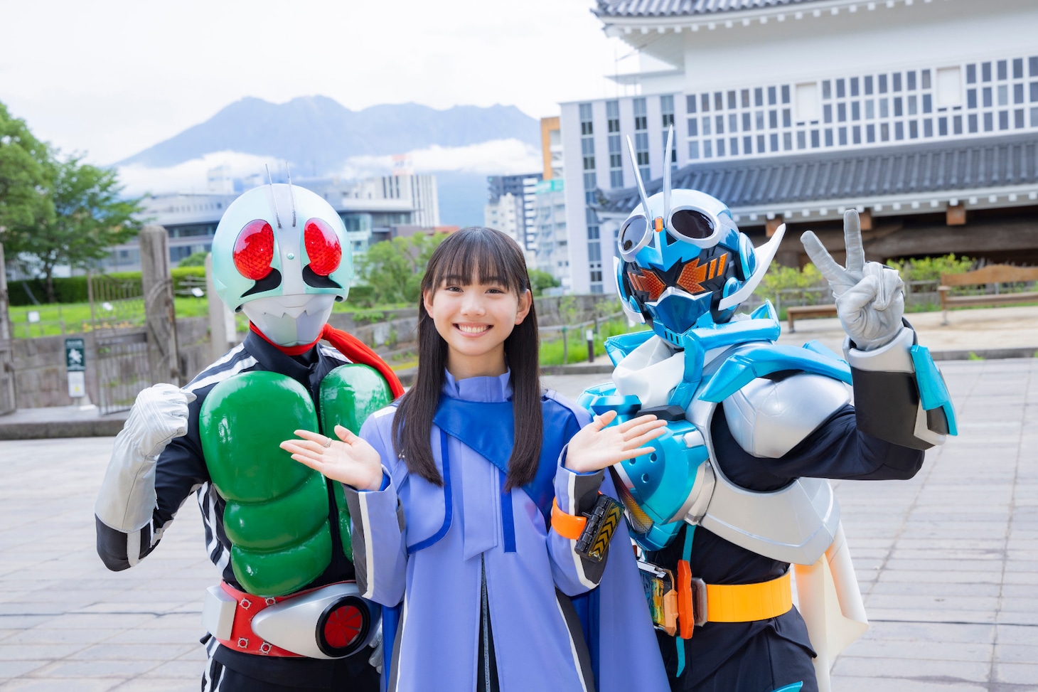 桜島をバックに仮面ライダー1号（左）と仮面ライダーガッチャード（右）と記念撮影をした松本麗世（中央）。